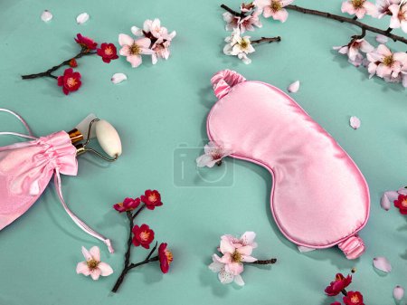 Photo for Quality of sleep, and self care routine. Sleeping mask, massage stone roller in silk bag with spring flowers on colored paper background - Royalty Free Image