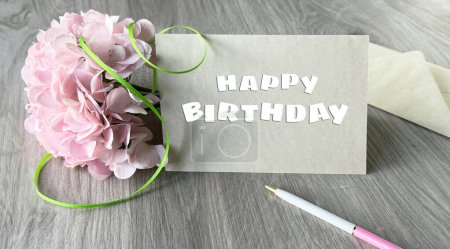 Foto de Una tarjeta de cumpleaños con un mensaje alegre, adornada con flores rosadas vibrantes y personalizada con un bolígrafo. - Imagen libre de derechos