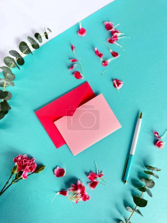 A photograph featuring a pink envelope with a note and a pen placed on a vibrant turquoise background. Copy-space on greeting card.