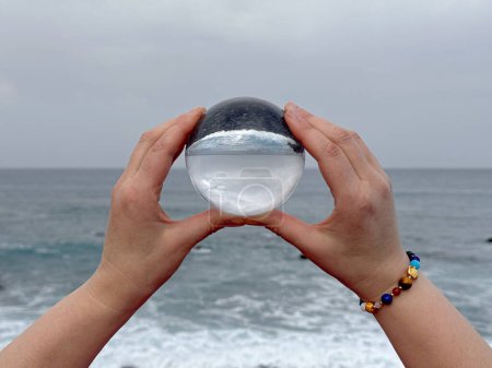 Photo for Hands holding crystal ball on ocean shore, meditation, spiritual journey, connection with Nature. - Royalty Free Image