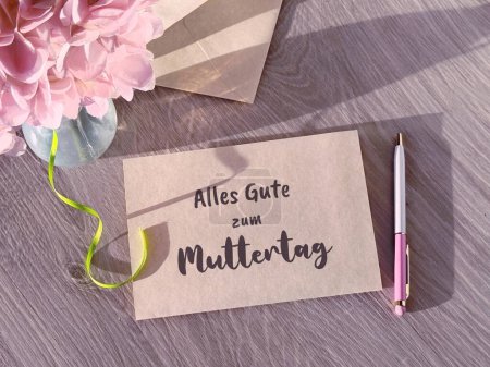 Une image d'un petit morceau de papier avec une note manuscrite Alles Gute zum Muttertag, or All the Best on Mother's Day in German attached to it.