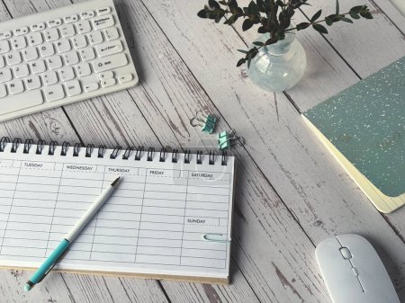 Photo for A desk with a blank weekly planner, keyboard and a mouse placed on it, ready for use. - Royalty Free Image