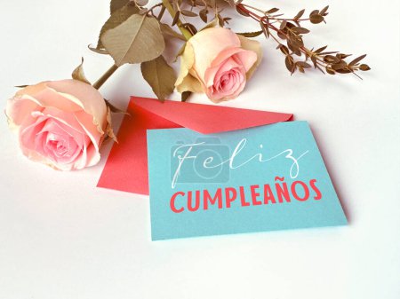 Foto de Una tarjeta con las palabras Felis Cumpleanos escritas en ella, o Feliz Cumpleaños en español, se coloca junto a un ramo de flores de gerberas rojas. - Imagen libre de derechos