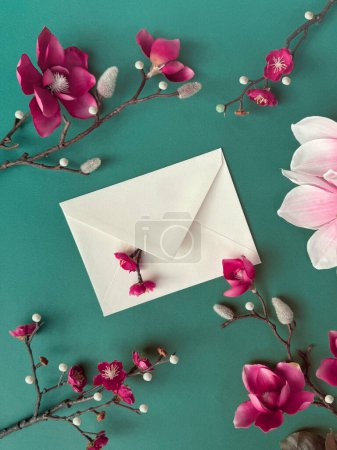 A white envelope decorated with delicate magnolia and plum pink flowers resting on a vibrant green background.