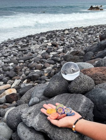 Photo for Hand holding chakra healing stones, glass and crystal ball on volcanic ocean shore. - Royalty Free Image