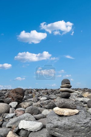 Téléchargez les photos : Pyramide en pierre zen sur un rivage volcanique sauvage avec ciel bleu et nuages. Méditation, voyage spirituel, harmonisation. - en image libre de droit