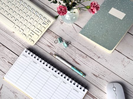 Téléchargez les photos : Un bureau avec un planificateur hebdomadaire vierge, un bloc-notes, un clavier, une souris et un bouquet de fleurs. - en image libre de droit
