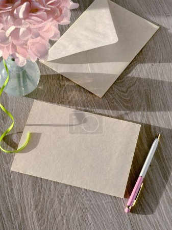 Photo for A table displaying a vase filled with flowers surrounded by two envelopes. Copy-space on blank greeting card. - Royalty Free Image
