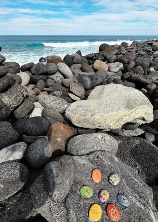 Foto de Cristales curativos, piedras de chakra. Gemas arco iris en un círculo en la orilla gris del océano volcánico. - Imagen libre de derechos