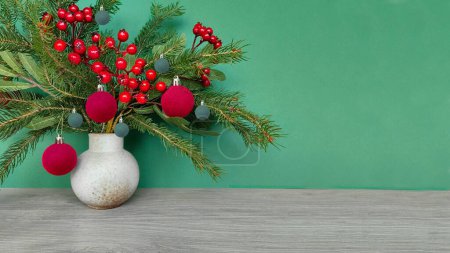 Foto de Arreglo de invierno con ramitas de abeto, decoraciones navideñas y bayas rojas de serbal en la mesa de madera junto a la pared verde. Imagen panorámica, espacio-copia. - Imagen libre de derechos