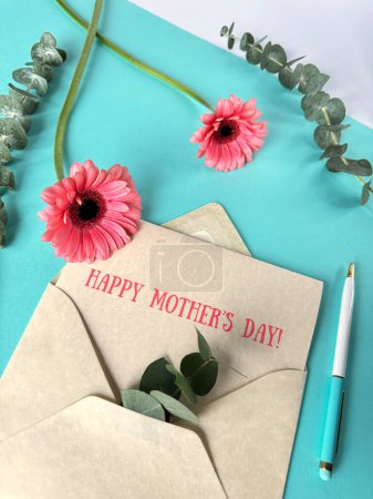 A photograph capturing a Mothers Day card featuring pink gerbera flowers on the front cover, placed next to an envelope.
