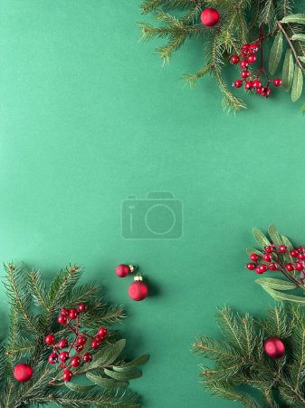 A festive green background adorned with vibrant red berries, greenery, fir twigs, and rowanberries. Baubles and Christmas decorations create a visually appealing composition with ample copy space.
