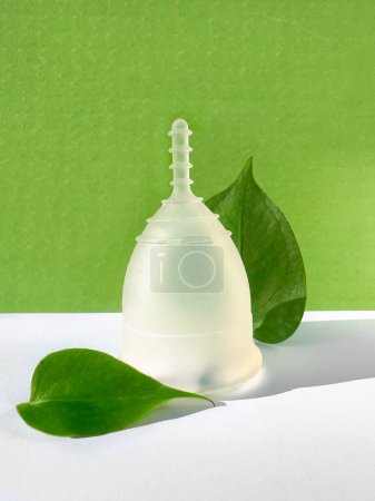 Photo for A reusable silicone menstrual cup with green leaf on a green colored paper background, an eco-friendly low impact menstruation product. - Royalty Free Image