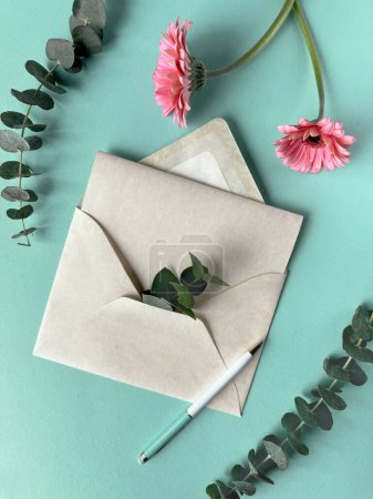 Ein mit rosa Gerbera-Blumen geschmückter Umschlag und darauf ein Stift. Kopierraum auf der Grußkarte.