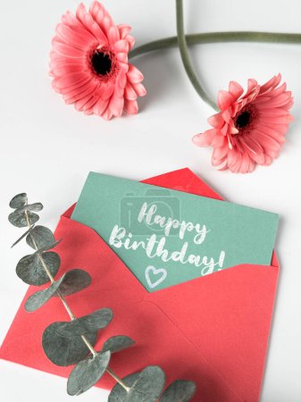 Photo for An image of a pink envelope with a vibrant happy birthday card placed on top of it with pink gerbera flowers. - Royalty Free Image