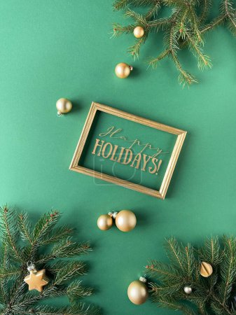 Photo for A vibrant green background decorated with festive holiday ornaments. The display includes fir twigs, golden baubles, and other Christmas decorations. A sign with the word Happy Holidays in frame. - Royalty Free Image