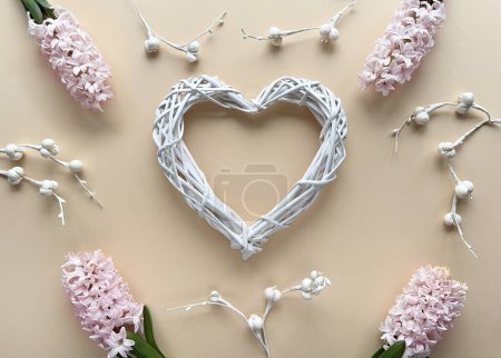 Foto de Un objeto en forma de corazón hecho a mano de material de mimbre, adornado con jacinto rosa y flores de papel blanco sobre fondo de papel amarillo. Mezcla de elementos naturales con artesanía artística. - Imagen libre de derechos