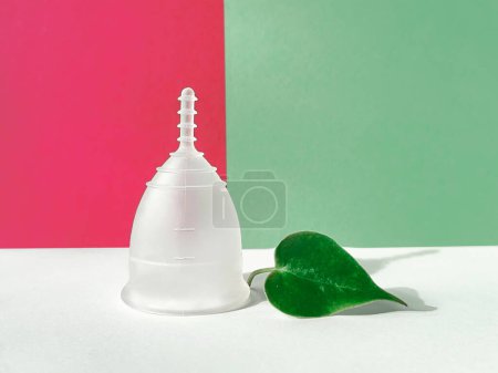 Foto de Una copa menstrual de silicona reutilizable con hoja verde sobre un fondo de magenta y papel verde, mostrando un producto de menstruación único y ecológico. - Imagen libre de derechos