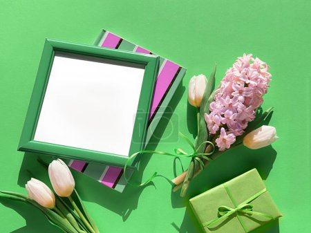 Photo for A picture frame and gift box are next to a fragrant bouquet of spring flowers, featuring white tulips and pink hyacinth in full bloom. - Royalty Free Image