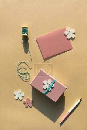 Photo for Pink gift box with wooden flowers, cyan cord reel, pen on orange paper. - Royalty Free Image