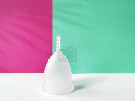 Eine wiederverwendbare Menstruationstasse aus Silikon auf magenta-grünem Papier, die ein einzigartiges und umweltfreundliches Menstruationsprodukt präsentiert.