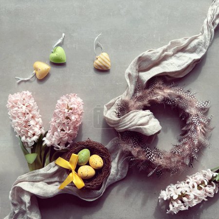 Photo for Quail feather wreath, pink hyacinth flowers, birds nest with Easter eggs, linen towel. Spring background with springtime decor on grey stone concrete background. - Royalty Free Image