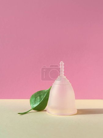 A reusable silicone menstrual cup with green leaf on a pink colored paper background, showcasing a unique and eco-friendly menstruation product.