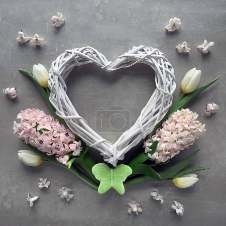 Foto de Una corona en forma de corazón con flores de primavera, tulipanes y jacinto, con una colorida mariposa de cerámica. - Imagen libre de derechos