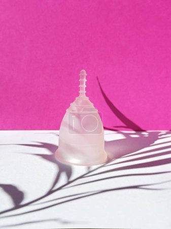 A reusable silicone menstrual cup with leaf shadow on a magenta paper background, showcasing a unique and eco-friendly menstruation product.