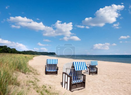 Photo for Wooden lawn chairs rest on a sandy beach, facing the vast ocean under the clear skies of a sunny day. Romantic shores of Baltic sea. - Royalty Free Image