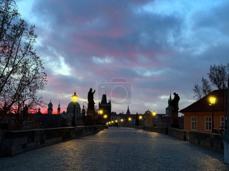 Téléchargez les photos : Pont Charles de Prague à l'aube : les réverbères brillent sous un ciel rose-gris. - en image libre de droit