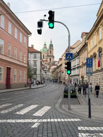 Foto de Praga, República Checa - 31 de marzo de 2024: Calle Cobbled en Mala Strana, Praga, República Checa, con la Iglesia de San Nicolás detrás. Un semáforo verde se encuentra al lado de una carretera. - Imagen libre de derechos