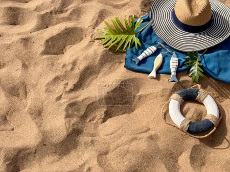 Beach Essentials: Hut, tropisches Blatt, Handtuch, Holzfischdekor und Rettungsring auf Sand.
