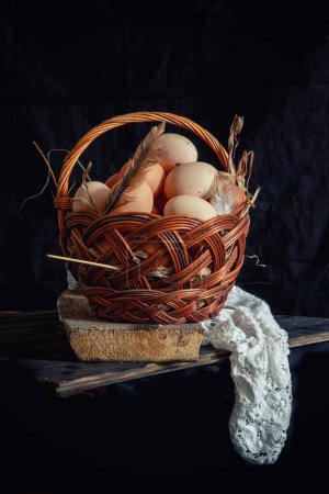 Téléchargez les photos : Œufs de poulet dans un panier en osier sur un fond sombre - en image libre de droit