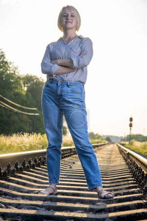 Photo for A woman in jeans is sitting on a railway track. - Royalty Free Image