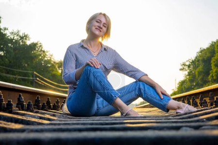 Photo for A woman in jeans is sitting on a railway track. - Royalty Free Image
