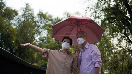 Photo for Asian senior elder couple walking in raining park share umbrella romantic love lifestyle - Royalty Free Image