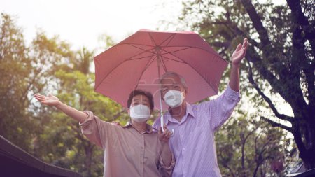Téléchargez les photos : Asiatique senior couple aîné marche dans la pluie parc partager parapluie romantique amour style de vie - en image libre de droit