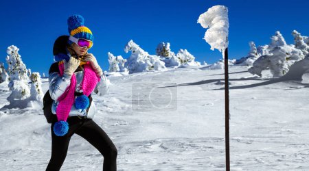Foto de Winter fashion. Beautiful girl is wearing jacket, ski goggles and colorful winter hat and is posing on mountains background. Szrenica, Poland. Mountain travel. - Imagen libre de derechos