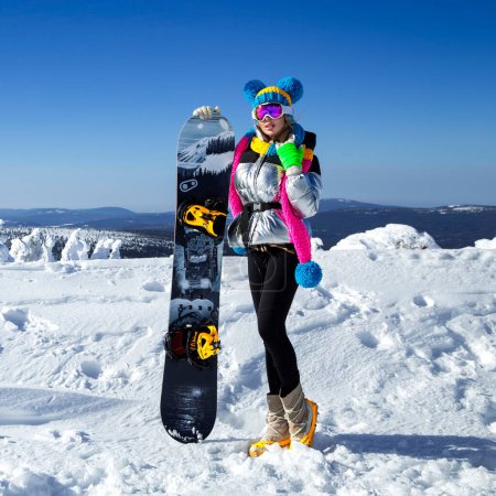Photo for Girl snowboarder enjoys the ski resort. Beautiful woman in winter outfit is posing with snowboard in the mountains. Winter sports. Snowboarding. - Royalty Free Image