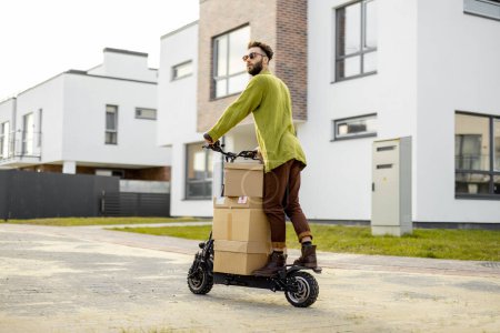 Foto de El hombre conduce scooter eléctrico, cajas de cartón de entrega en la calle en la zona residencial. Concepto de sostenibilidad, entrega y estilo de vida moderno ecológico - Imagen libre de derechos