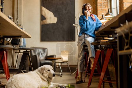 Foto de Woman sits with her cute adorable dog at modern coffee shop and works on laptop. Pet friendly places and modern digital lifestyle concept - Imagen libre de derechos