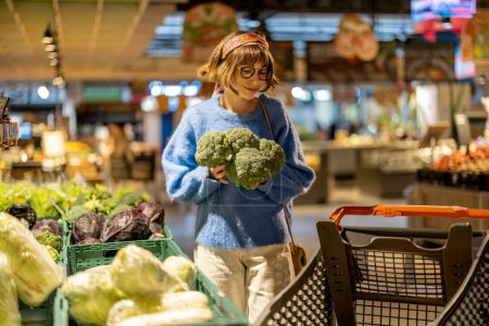 Photo for Young woman chooses broccoli, buying vegetables in supermarket. Concept of shopping groceries and healthy lifestyle - Royalty Free Image