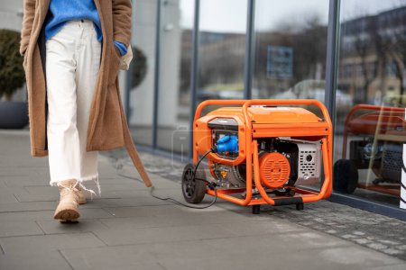 Photo for Female person walks on a street near office or shop supplied energy from gasoline generator. Concept of backup power supply and blackout - Royalty Free Image