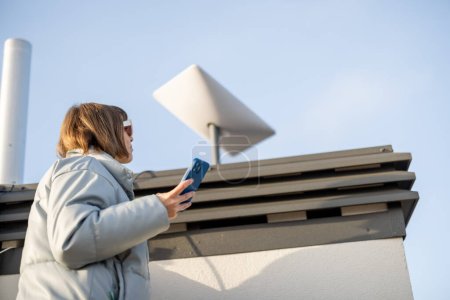 Foto de LVIV, UKRAINE - January, 2023: Woman installing Starlink satellite dish on roof of her house. Starlink is a satellite internet constellation operated by SpaceX - Imagen libre de derechos