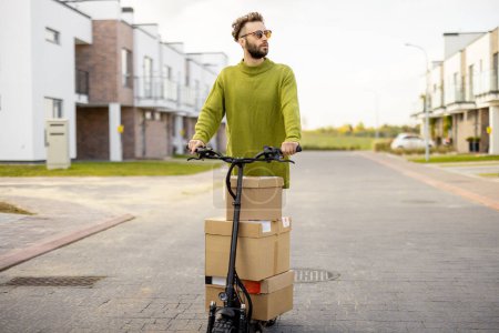 Foto de El hombre conduce scooter eléctrico, cajas de cartón de entrega en la calle en la zona residencial. Concepto de sostenibilidad, entrega y estilo de vida moderno ecológico - Imagen libre de derechos