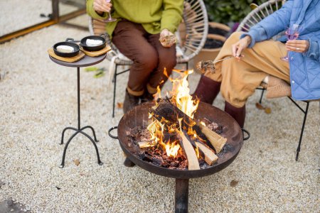 Burning fire in fire bowl with chairs and table in backyard. Cozy atmosphere for dining during autumn time