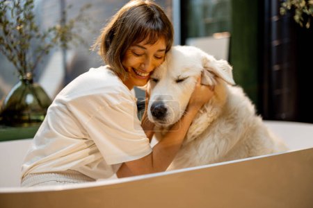 Téléchargez les photos : Portrait of a young woman with her cute dog in bathtub. Woman hugs with pet before washing. Concept of friendship with pets and care - en image libre de droit