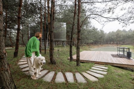 Foto de Woman walks on wavy pathway near lake and invisible cabin in pine forest. Connection with nature and sustainability concept. Rest in tiny cabins on nature - Imagen libre de derechos