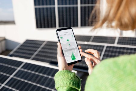 Foto de Woman monitors energy production from the solar power plant with mobile phone. Close-up view on phone screen with running program. Concept of remote control of solar energy production - Imagen libre de derechos